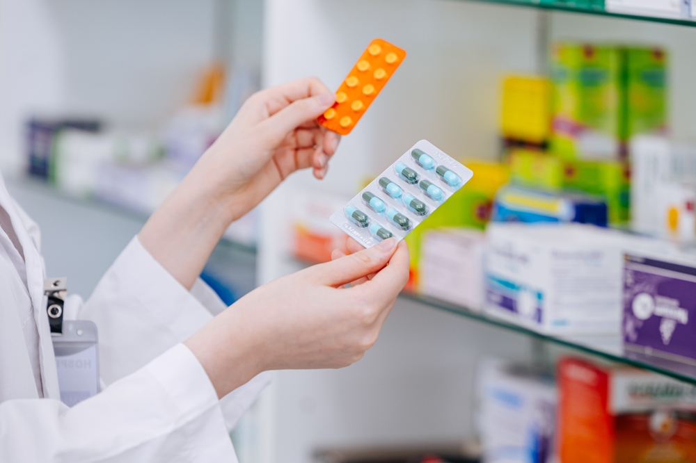 Pharmacist comparing two blister packs of pills in a pharmacy, illustrating review of medications that may trigger Stevens-Johnson Syndrome