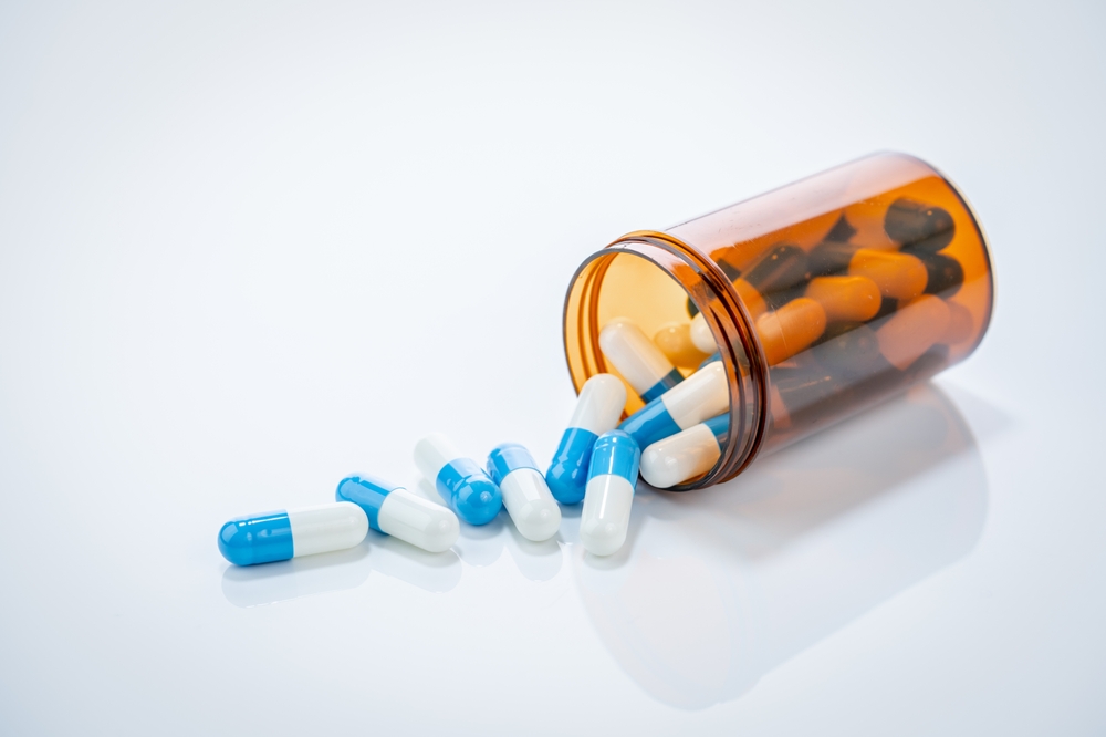 Blue and white capsules spilling from an orange prescription bottle, illustrating drugs that may cause Stevens-Johnson Syndrome.
