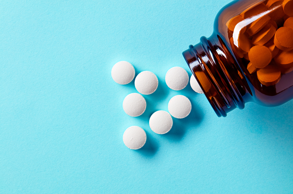 White tablets spilling from a brown bottle on a blue background, illustrating drugs that may cause Stevens-Johnson Syndrome and potential legal action.